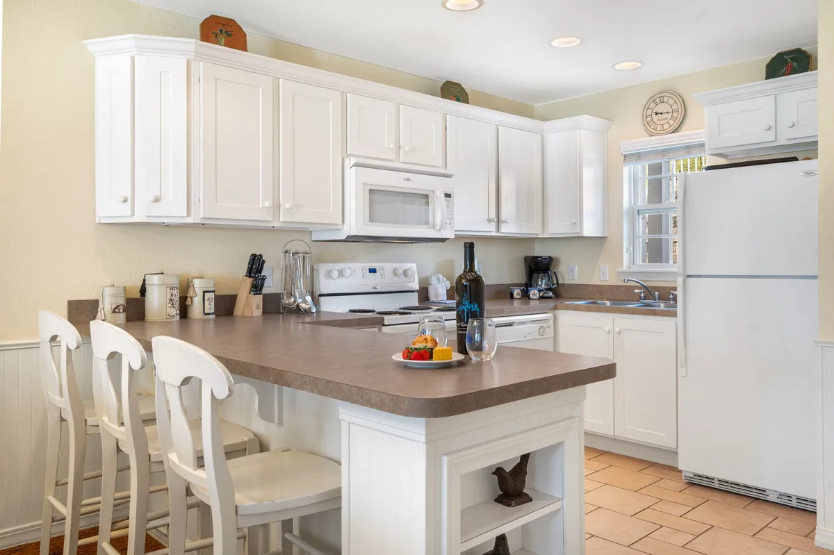 The image showcases a bright, inviting kitchen island at the heart of the condo. The island features comfortable seating, a wine bottle with glasses ready for toasting, and a colorful bowl of fresh fruit, suggesting the space is perfect for cooking, entertaining, and gathering with loved ones.