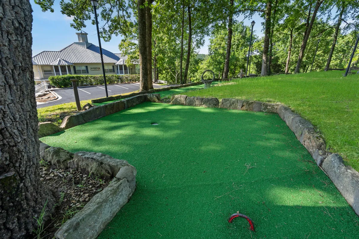 A playful miniature golf area flanked by trees and a playground, creating an inviting space for families. The green putting area and nearby playground equipment suggest lively, cheerful, and inclusive recreational opportunities for guests of all ages.