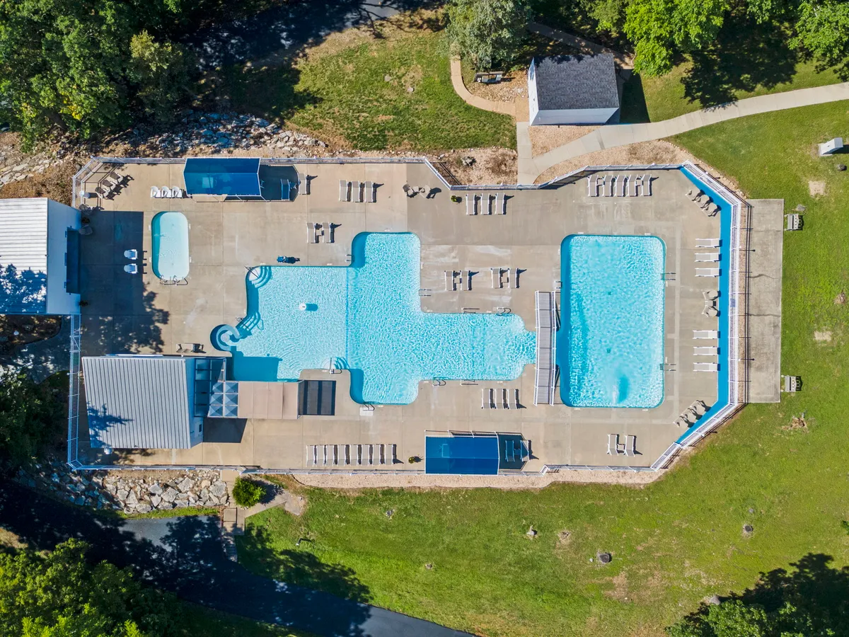 A bright, inviting outdoor pool area surrounded by greenery. Sun loungers are set up on the pool deck, offering spots for relaxation and socializing. The scene exudes a relaxed vacation vibe, ideal for sunny afternoons or unwinding after a swim.