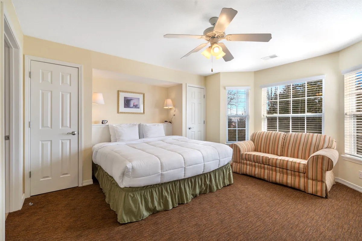 A cozy king bedroom featuring a large bed with a striped sofa beside it, ample windows letting in natural light, and a relaxing, intimate atmosphere perfect for unwinding.