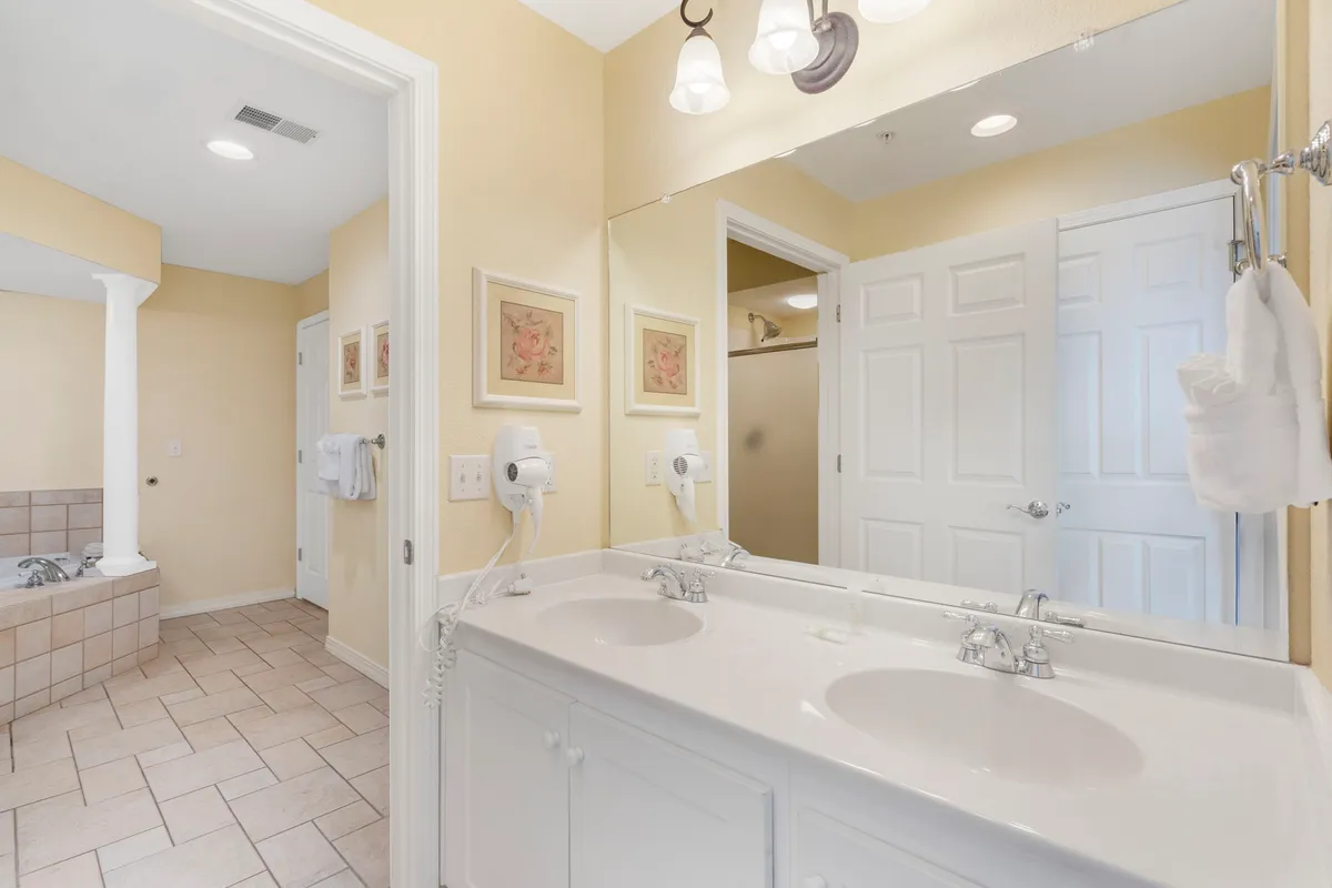 A bright ensuite bathroom with a double sink vanity, a deep bathtub, large mirror, and decorative wall art, conveying a spa-like, inviting atmosphere ideal for self-care routines.
