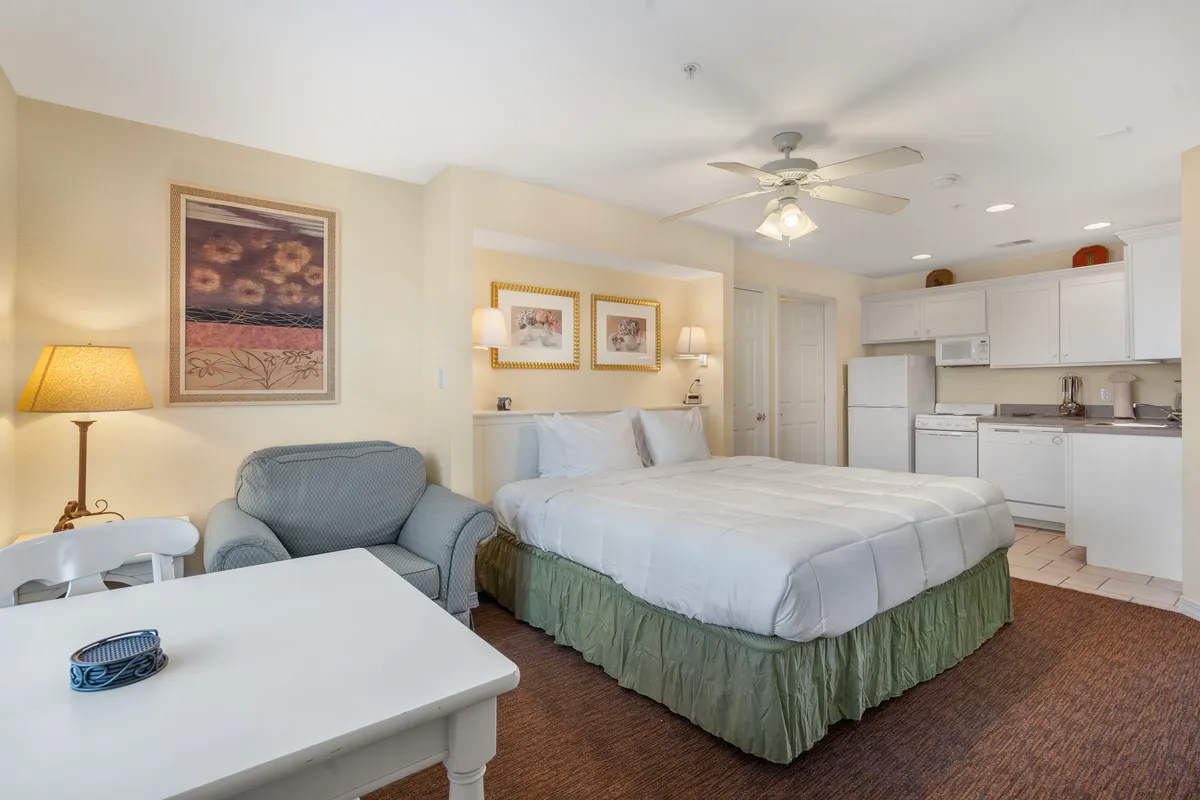 A spacious interior suite with a king bed, comfortable sofa, table, and a compact kitchen area in the background, styled with tasteful artwork for a homey, multi-functional feel.