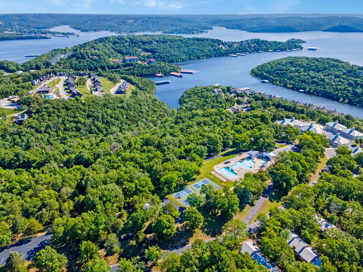 An exterior shot capturing lush greenery, a sparkling swimming pool, tennis courts, and a waterfront view of Table Rock Lake. The space is inviting for swimming, playing tennis, or simply relaxing by the water.