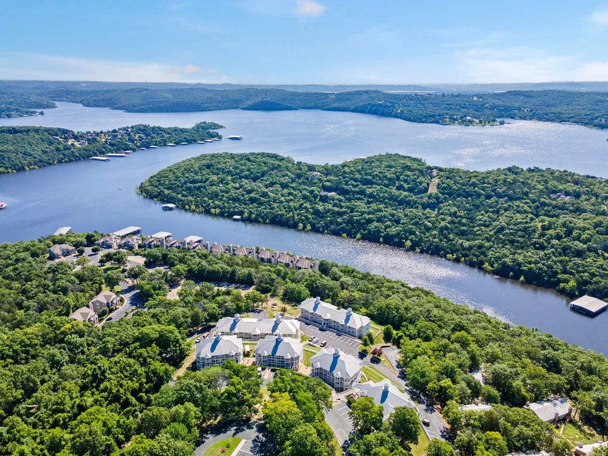 A sweeping view of an expansive water body with a lush green landscape and well-maintained resort buildings in the distance. The scene suggests opportunities for hiking, nature walks, and lakeside strolls, with visible walking paths and open green spaces.