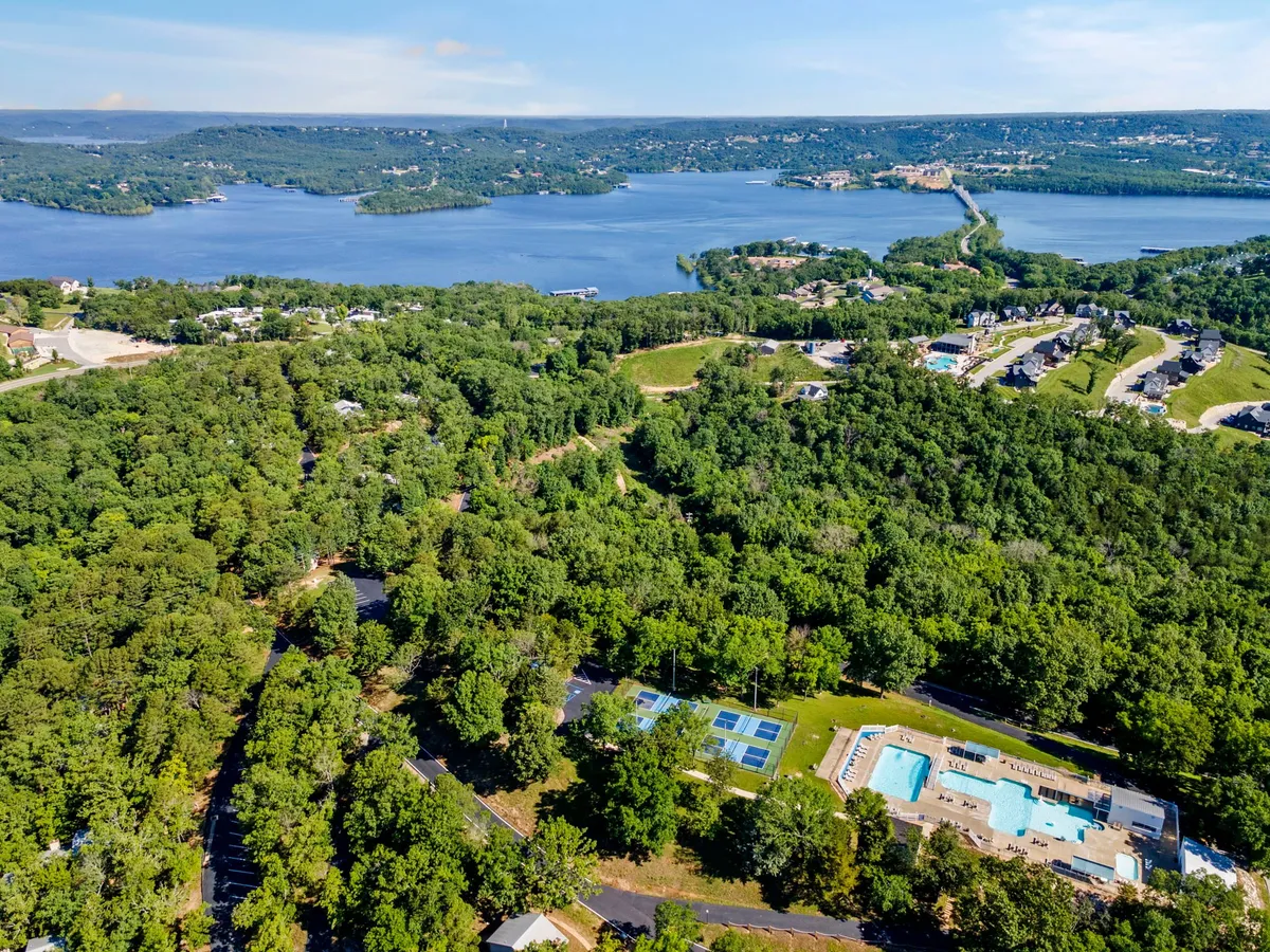 A panoramic vista of a lake framed by swimming pools, tennis courts, and abundant greenery. The area features paths and recreational amenities that invite exploration, relaxation, and pet-friendly walks.